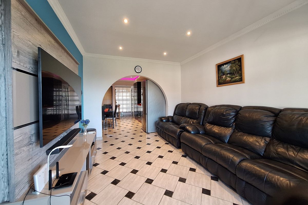 A living room featuring tiled flooring, recessed ceiling lighting, and a decorative arched entryway leading to the adjacent dining area.
