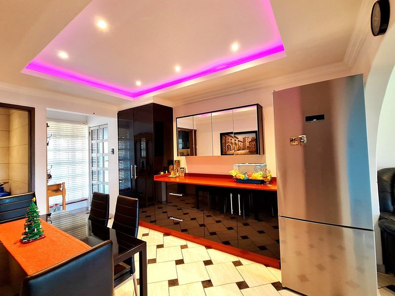Open plan dining and kitchen area featuring high-gloss cabinetry, recessed tray ceiling with integrated LED lighting, and tiled flooring.
