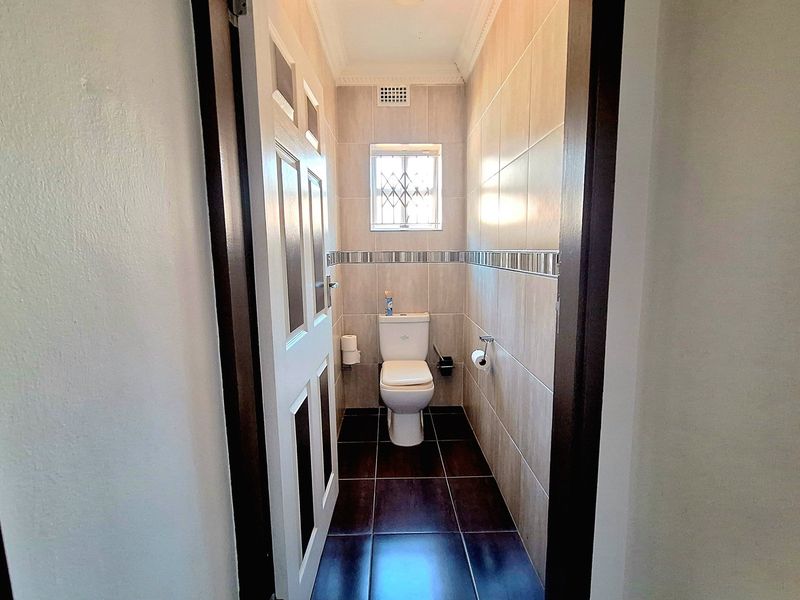 A compact, tiled guest bathroom featuring a modern toilet, neutral wall tiles, and a security-grille window.