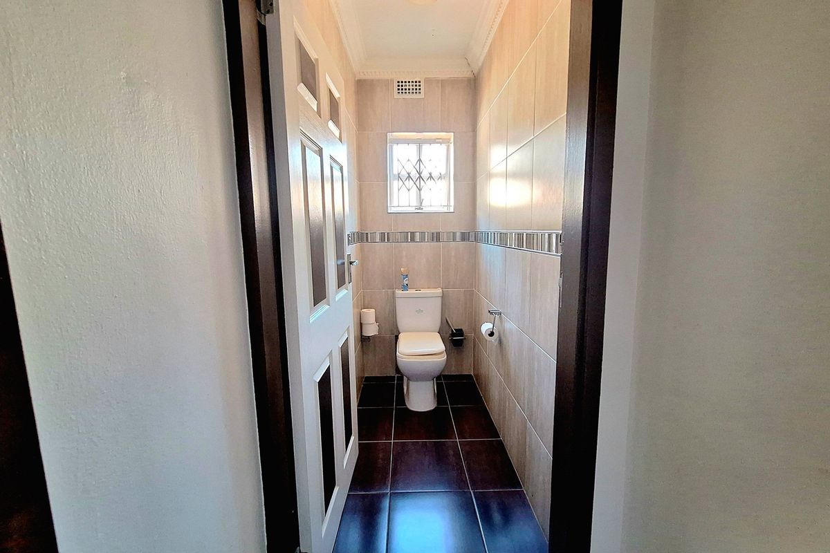 A compact, tiled guest bathroom featuring a modern toilet, neutral wall tiles, and a security-grille window.