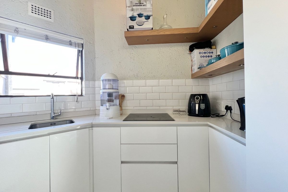 Modern kitchen featuring white cabinetry, stone countertops, subway tile backsplash, integrated induction hob, and floating timber shelving.
