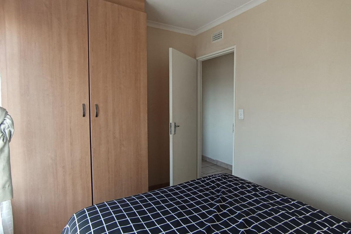 A bedroom featuring built-in wooden cupboards and a doorway leading to an adjacent tiled area.