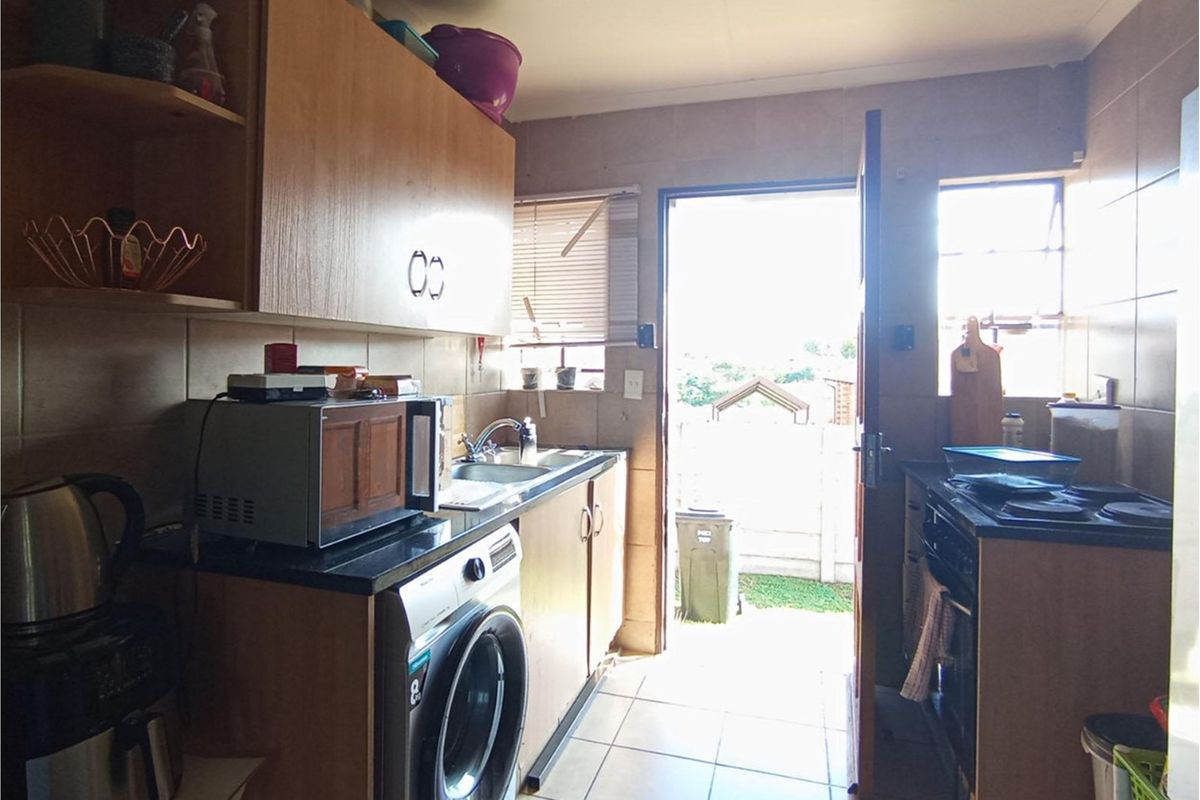 A functional kitchen featuring built-in wooden cabinetry, tiled splashbacks, a stainless steel sink, and direct access to the exterior.