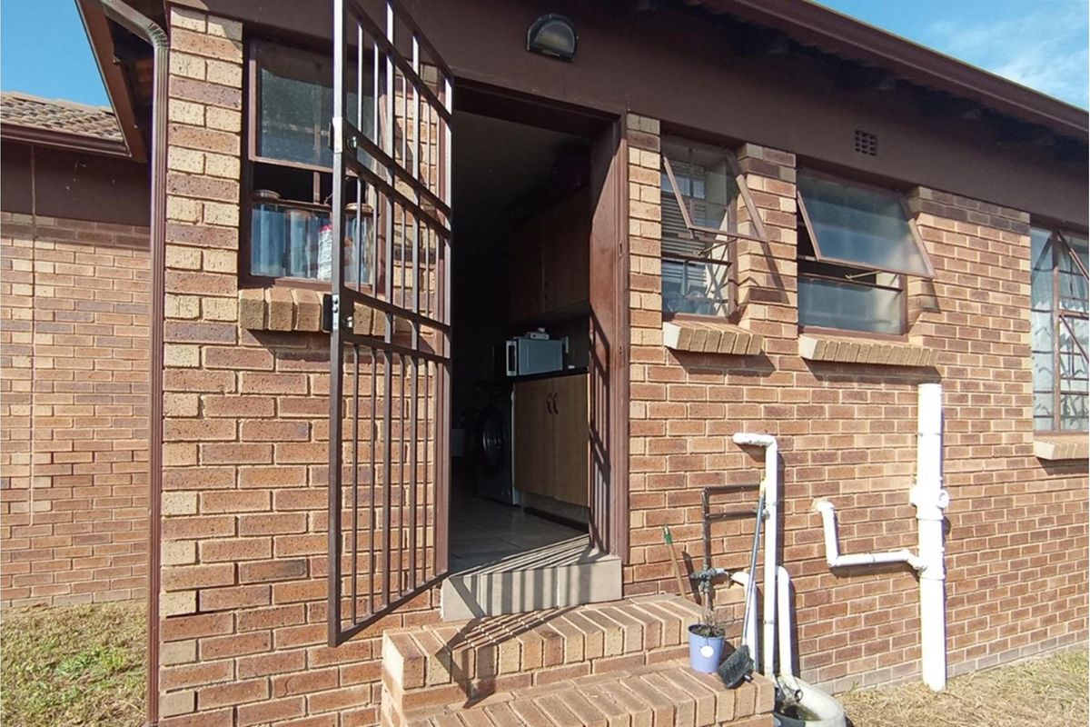 Exterior view of a townhouse rear entrance featuring face-brick construction, security gate, and visible utility plumbing connections.