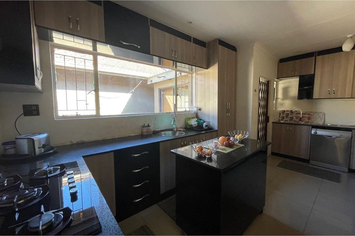 A functional kitchen featuring dark stone countertops, two-tone cabinetry, a central island, and a built-in gas hob with an integrated sink area.