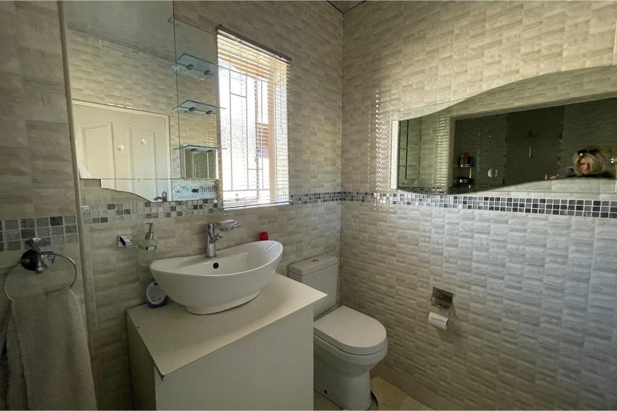 A compact bathroom featuring a modern vessel sink, vanity cabinet, wall-mounted mirror, and tiled walls with a decorative mosaic border.