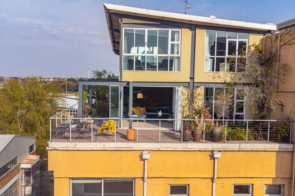 An elevated view of a modern apartment featuring a spacious balcony with metal railings and large glass sliding doors leading into the living area.