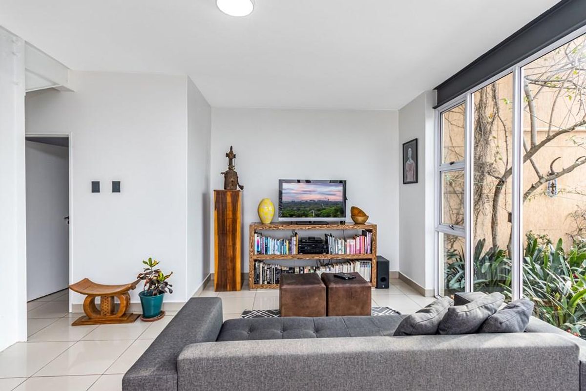 Bright living room featuring large floor-to-ceiling windows with views of the garden, tiled flooring, and neutral wall finishes.