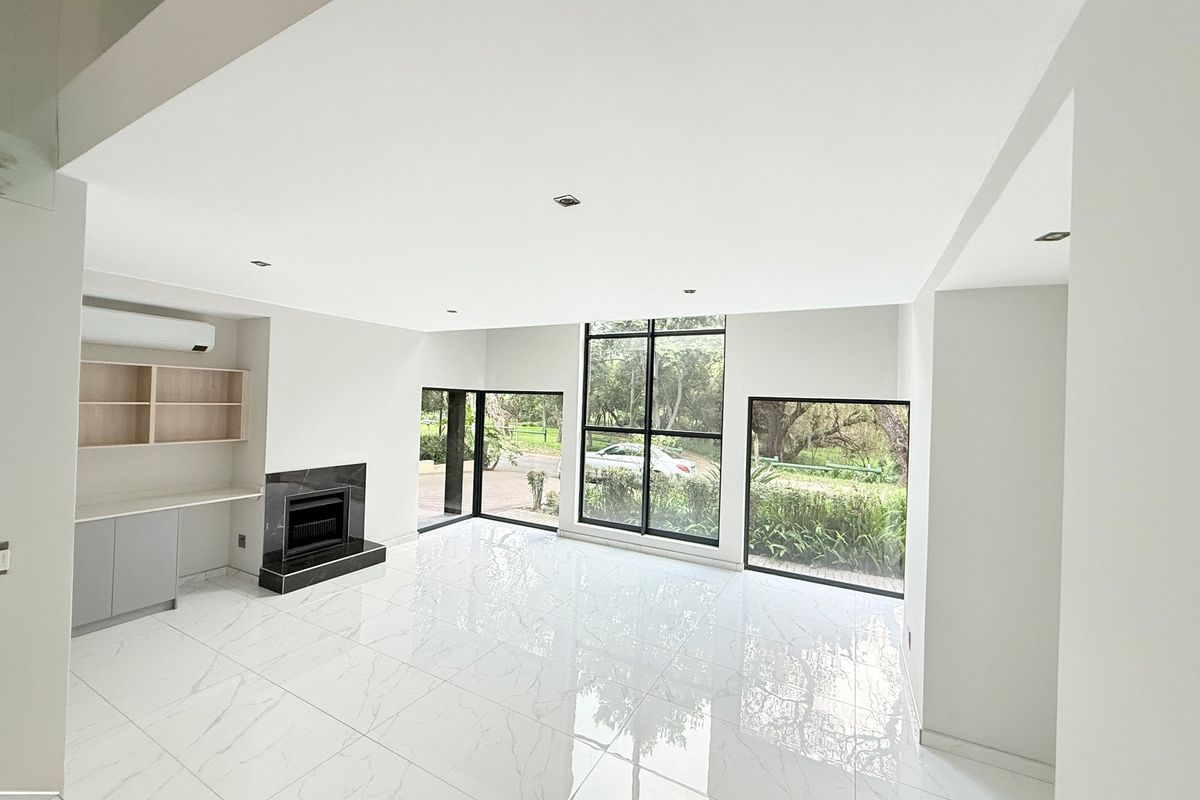 Bright and modern living area featuring large floor-to-ceiling windows, polished marble-look tile flooring, a built-in fireplace, and integrated shelving.