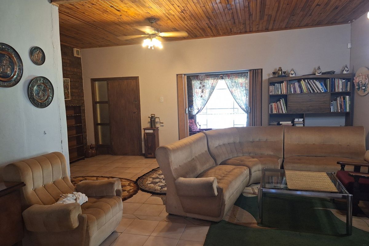 Spacious living room featuring a timber-clad ceiling, tiled flooring, and a brick feature wall, offering a traditional and comfortable living space.