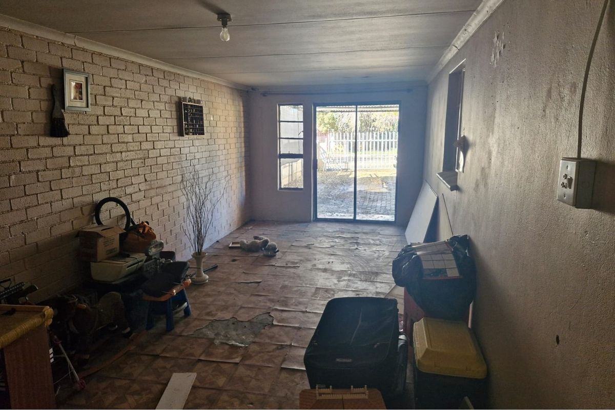 A living area featuring an exposed brick wall, sliding glass door access to the garden, and significant wear to the flooring and wall finishes.