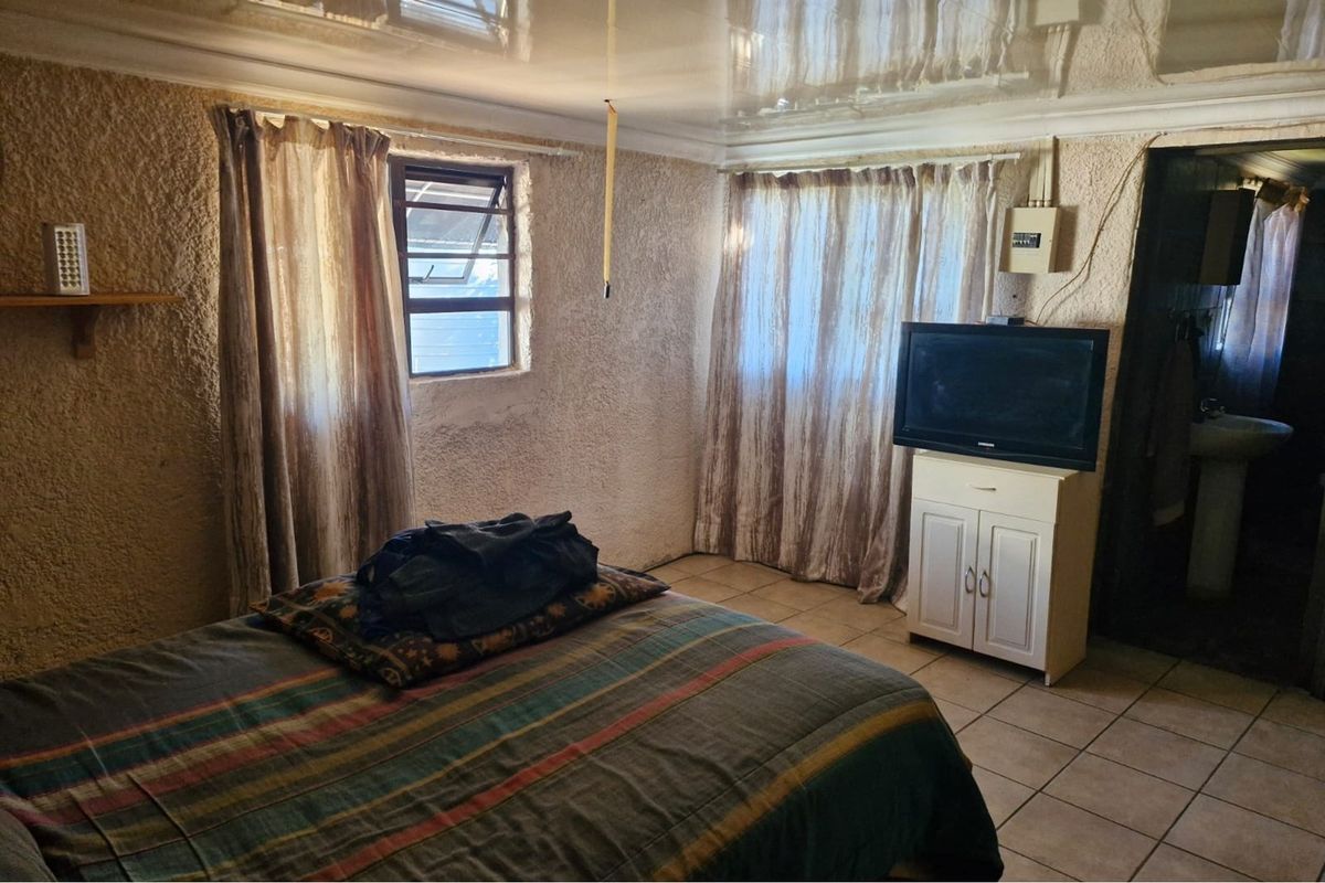 A bedroom featuring tiled flooring, textured walls, and a glossy ceiling finish, with a louvered window providing natural light.
