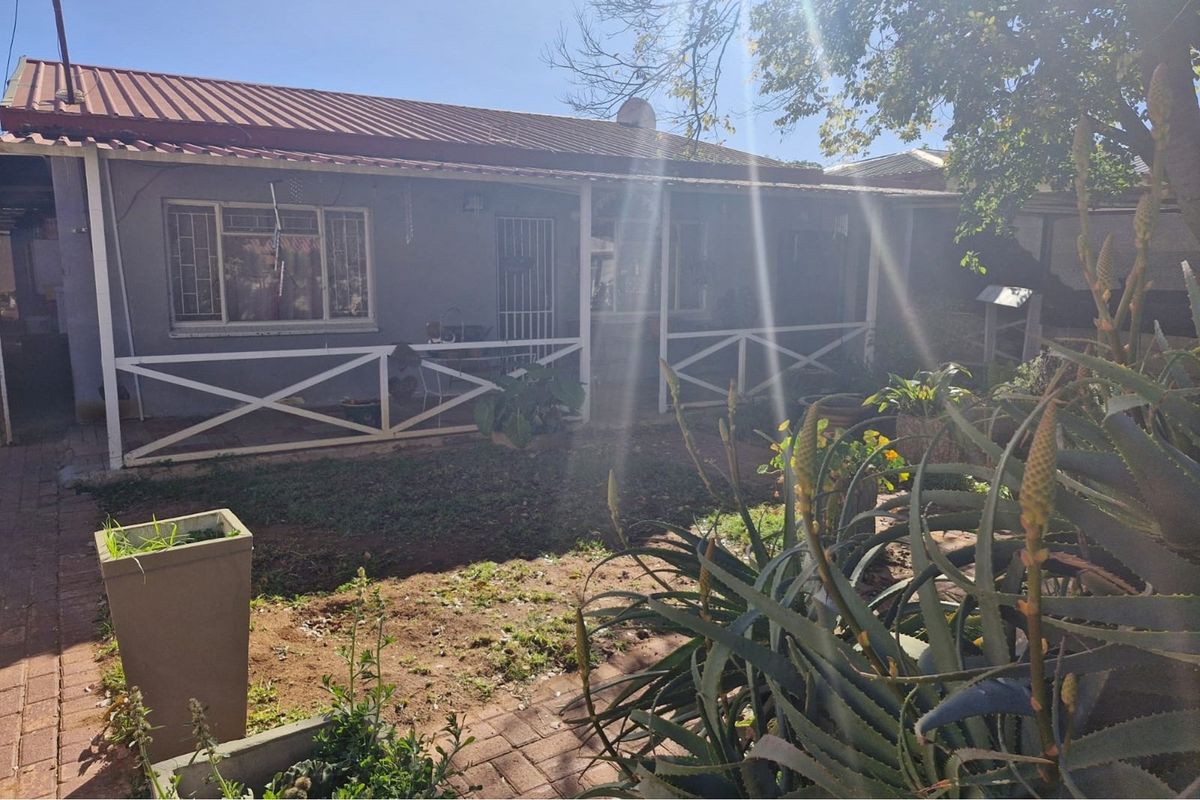 Rear view of the house featuring a covered patio with timber balustrades, metal window frames, and a garden area with paved pathways.