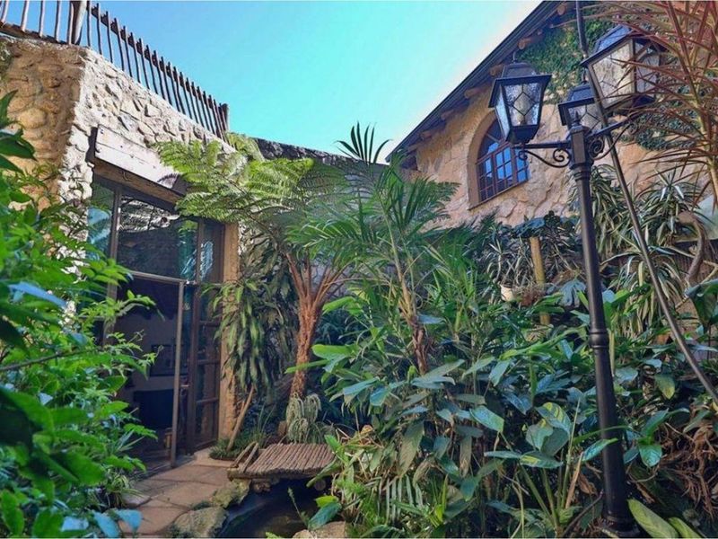 A charming, lushly landscaped rear courtyard featuring natural stone walls, an arched window, and a classic ornamental lamp post.