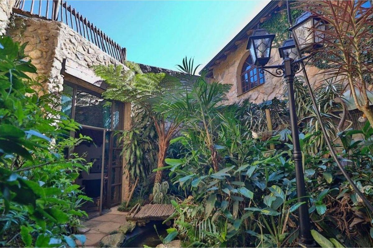 A charming, lushly landscaped rear courtyard featuring natural stone walls, an arched window, and a classic ornamental lamp post.
