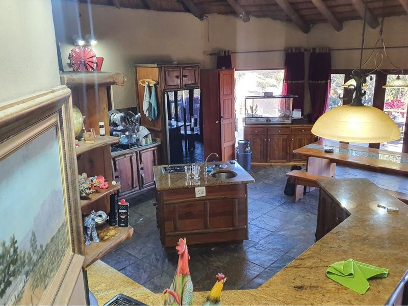 Spacious open-plan kitchen and dining area featuring rustic wooden cabinetry, granite countertops, slate flooring, and exposed timber beams under a traditional thatch roof.