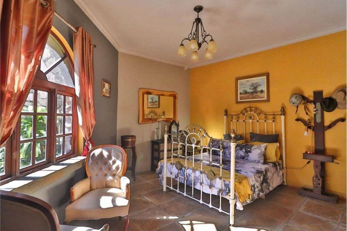 A bedroom featuring tiled flooring, an arched timber window, and warm-toned wall finishes.