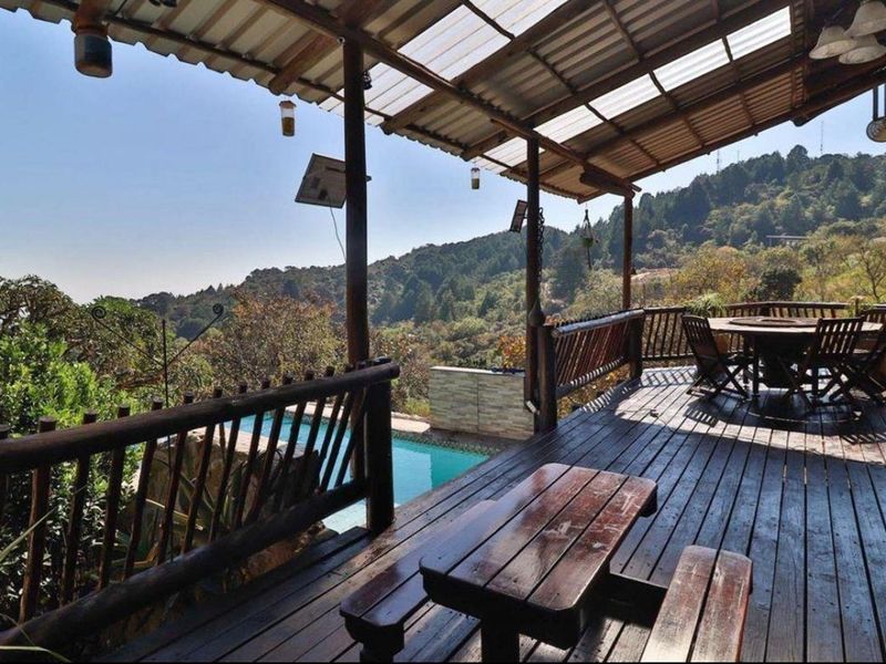 Spacious covered timber deck featuring a rustic railing, overlooking a swimming pool with scenic mountain landscape views.
