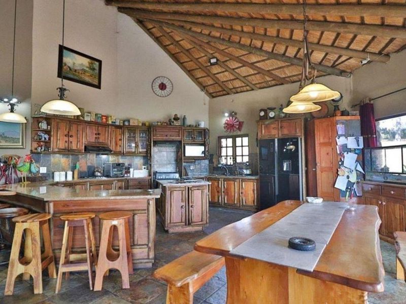 Spacious rustic kitchen featuring a high thatched ceiling with exposed beams, custom wooden cabinetry, granite countertops, and stone tile flooring.