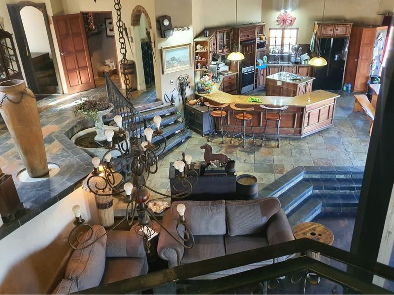 Spacious open-plan living and kitchen area featuring slate tile flooring, a central kitchen island with breakfast bar, and a rustic staircase.