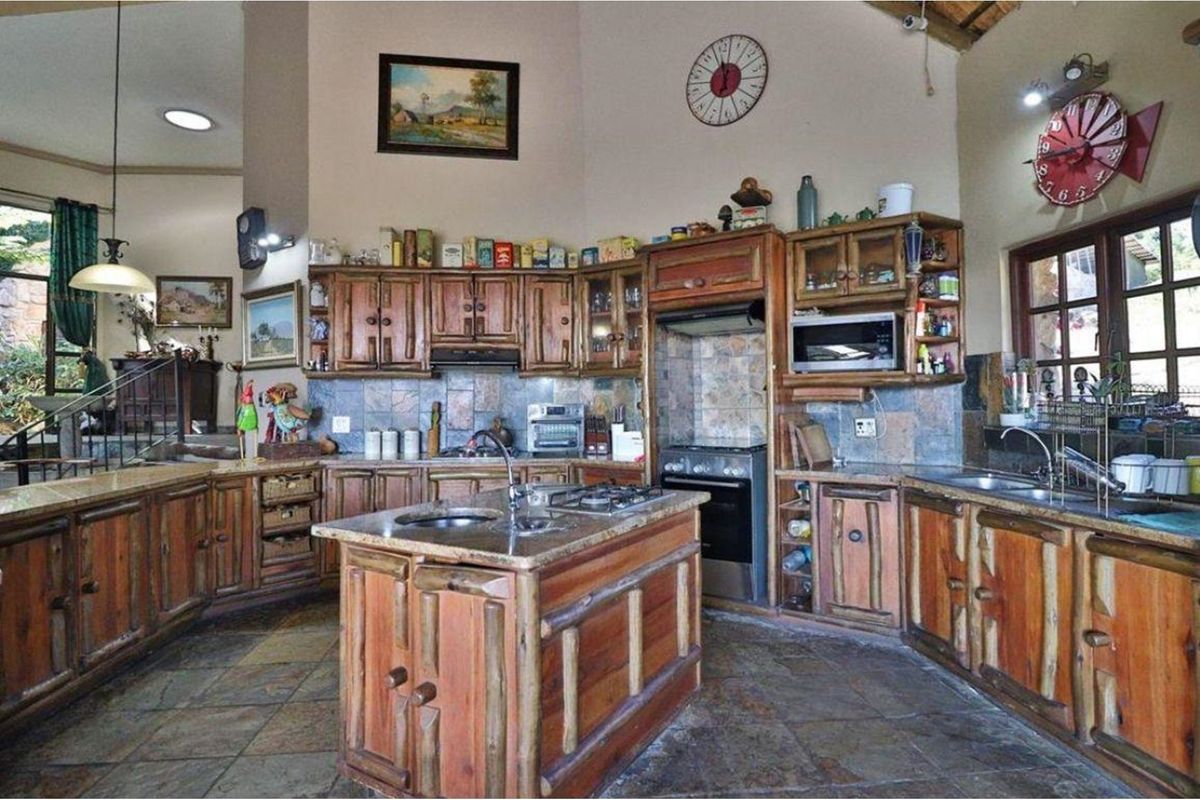 Spacious rustic kitchen featuring custom timber cabinetry, stone tile finishes, a central island with a sink, and a high vaulted ceiling.