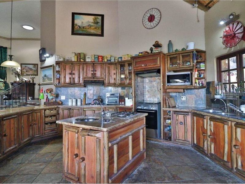 Spacious rustic kitchen featuring custom timber cabinetry, stone tile finishes, a central island with a sink, and a high vaulted ceiling.