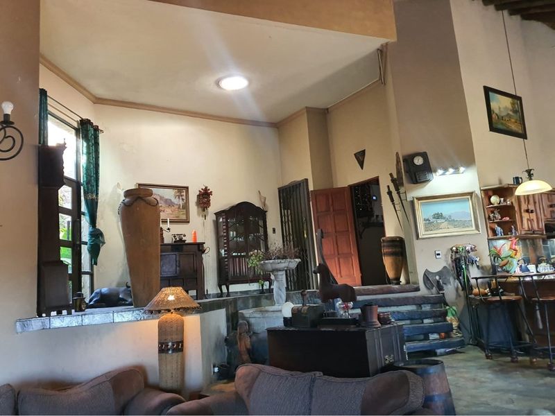 Spacious open-plan living area featuring vaulted ceilings, stone flooring, and a raised platform, offering a rustic farm-style aesthetic with integrated cabinetry and architectural character.