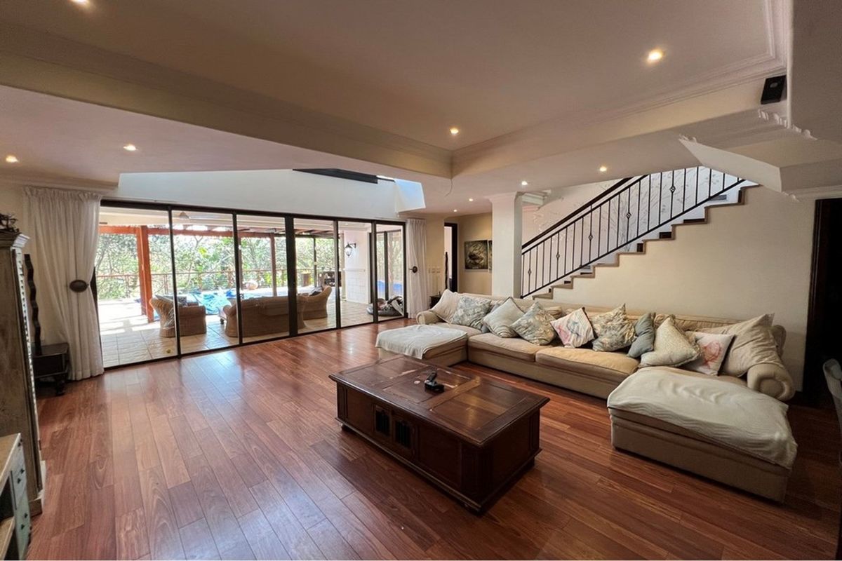 Spacious living room featuring rich hardwood flooring, recessed lighting, and a feature staircase with wrought iron railing, opening onto an outdoor patio area.