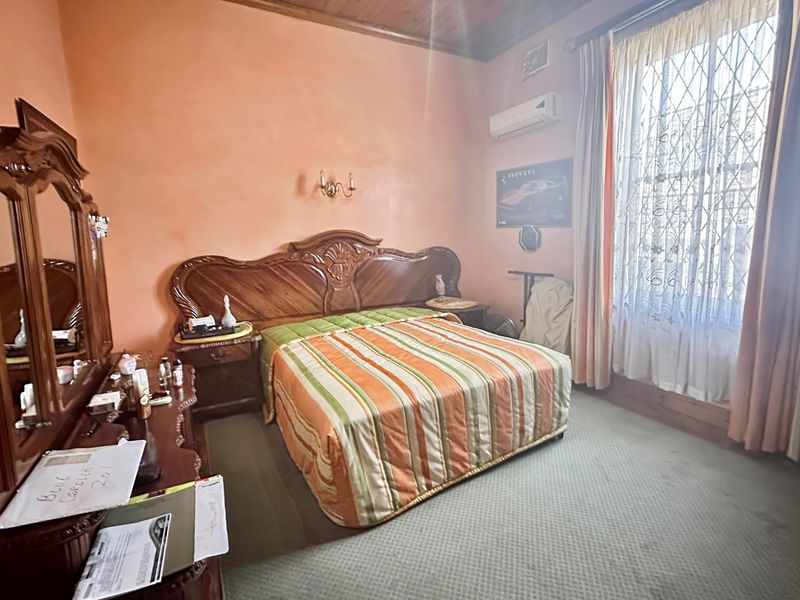 A bedroom featuring a timber ceiling, wall-mounted air conditioning unit, and large window with security bars.