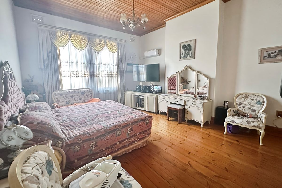 Spacious bedroom featuring polished timber flooring, a high timber-paneled ceiling, and a wall-mounted air conditioning unit.