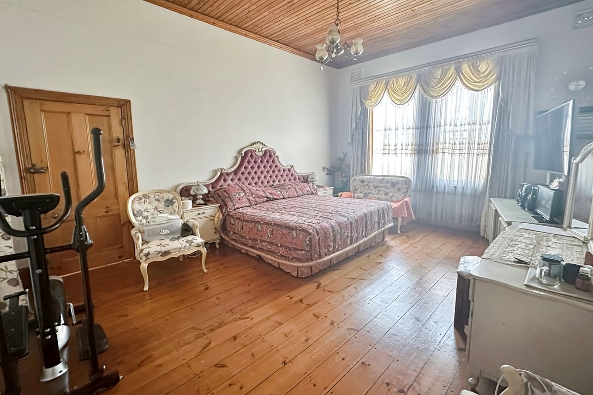Spacious bedroom featuring original timber flooring, high timber-paneled ceilings, and large windows allowing for ample natural light.