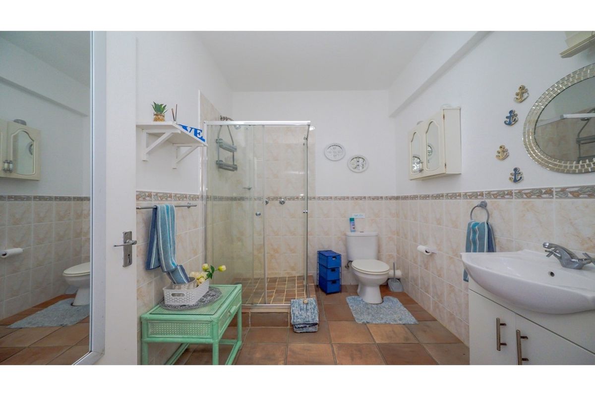 A functional bathroom featuring a glass-enclosed shower, a pedestal vanity with basin, and a standard toilet, finished with neutral wall and floor tiles.