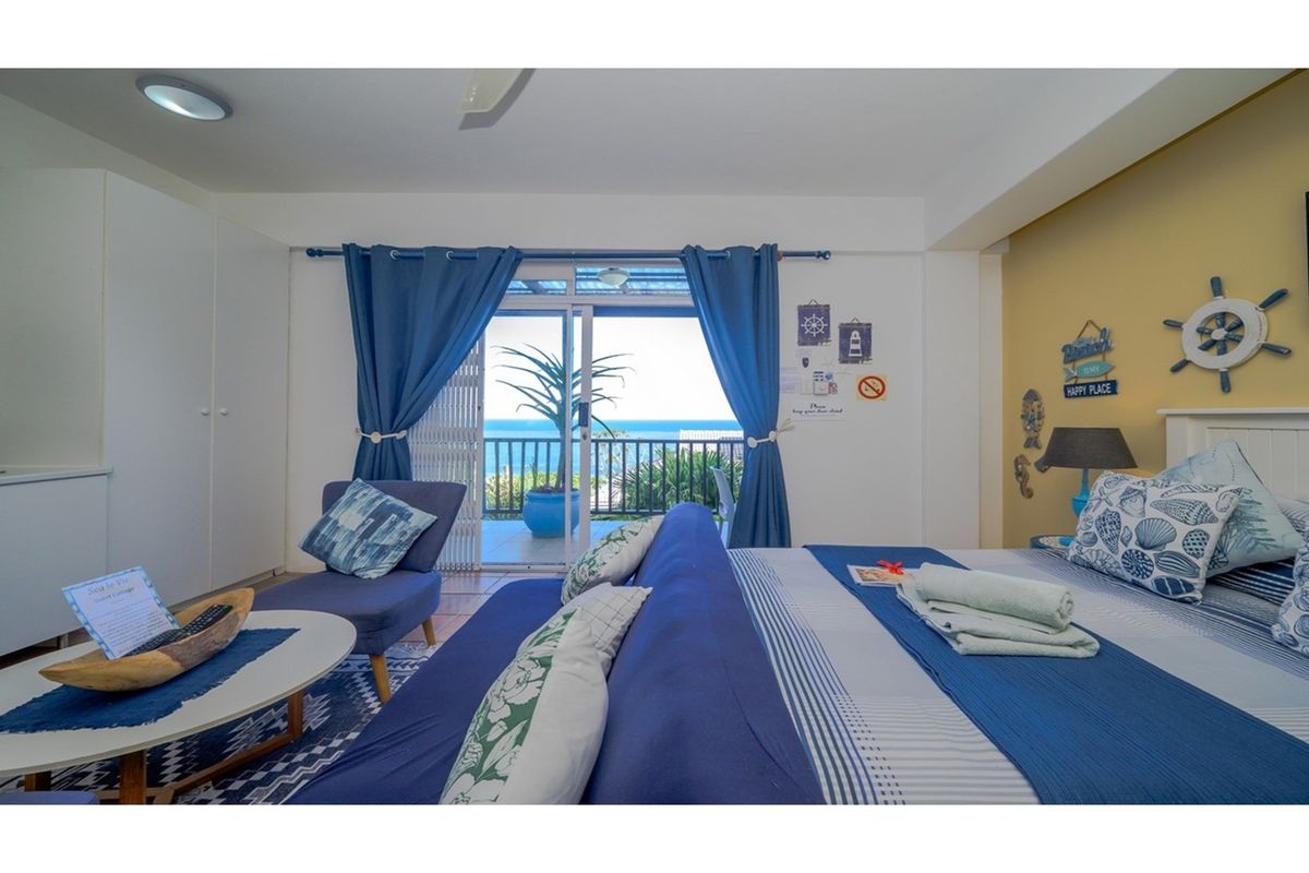 A bright bedroom featuring built-in cupboards and sliding glass doors that open onto a balcony with ocean views.