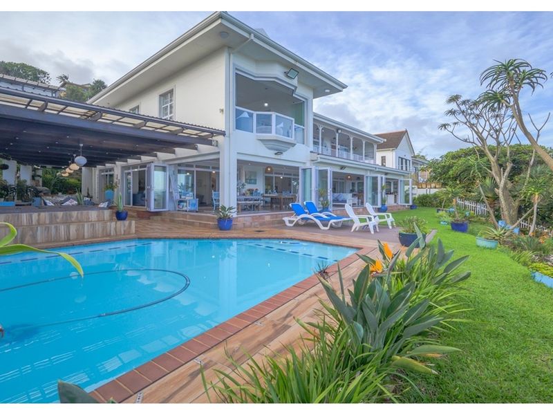 Spacious rear exterior featuring a swimming pool, tiled pool deck, covered patio area, and landscaped garden with established trees.