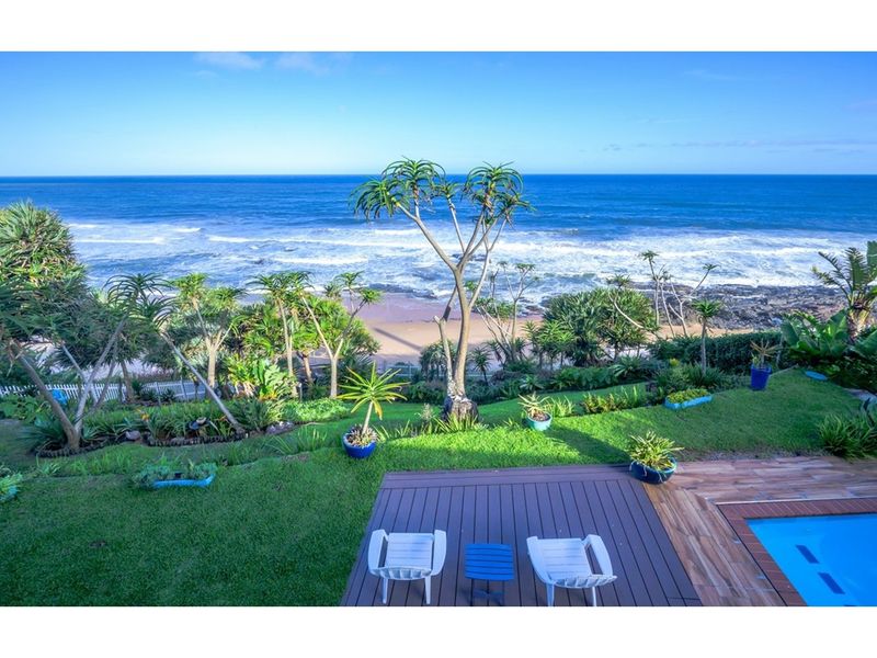 Elevated view of a landscaped garden, wooden deck, and swimming pool overlooking the ocean and coastline.