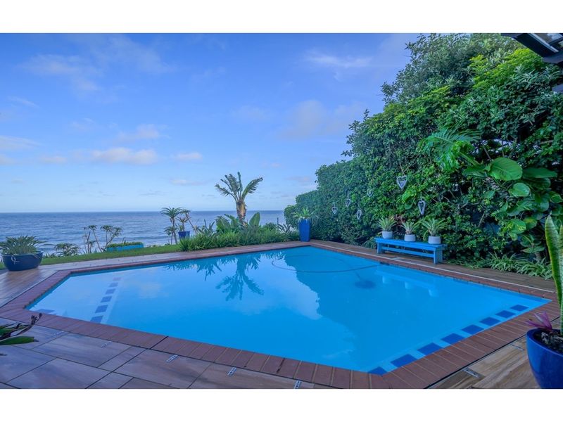 A well-maintained swimming pool area featuring a tiled deck and expansive ocean views, surrounded by lush garden landscaping.
