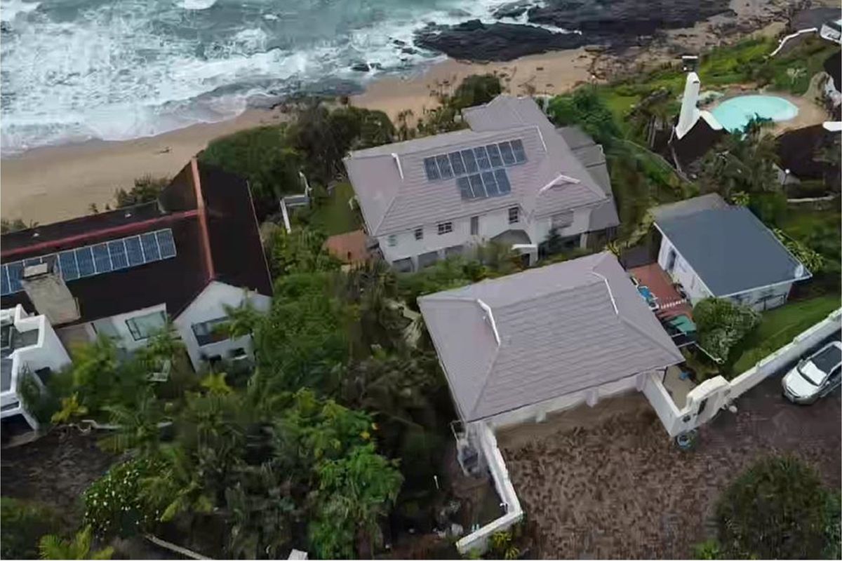 Aerial view of a coastal residential property featuring tiled roofs, solar panel installations, and proximity to the beach.