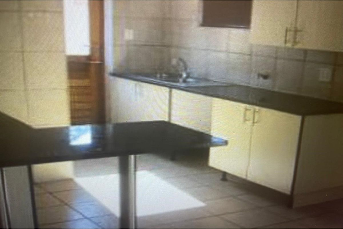 A functional kitchen featuring built-in cabinetry, dark countertops, tiled splashbacks, and a breakfast bar area with direct access to the exterior.