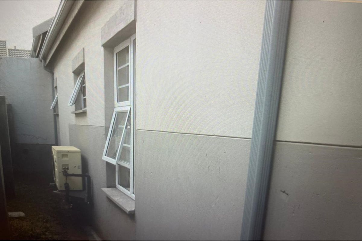 Side exterior view of the townhouse featuring painted masonry walls, white framed casement windows, and a vertical downpipe.