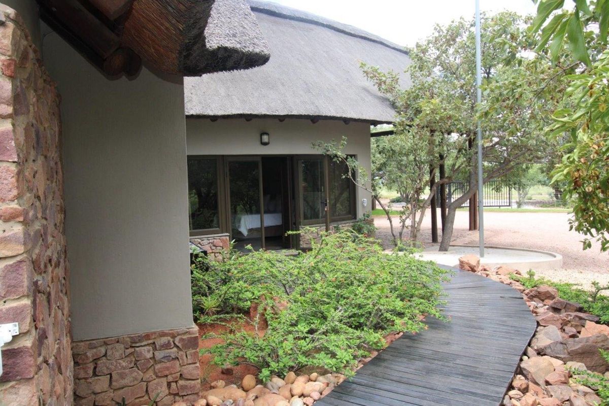 Exterior view of a thatched-roof dwelling featuring stone masonry accents, a wooden walkway, and landscaped garden surroundings.
