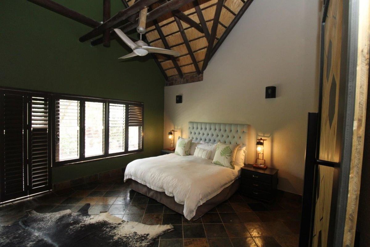 Spacious bedroom featuring a high vaulted thatched ceiling with exposed timber beams, tiled flooring, and large windows with integrated shutters.