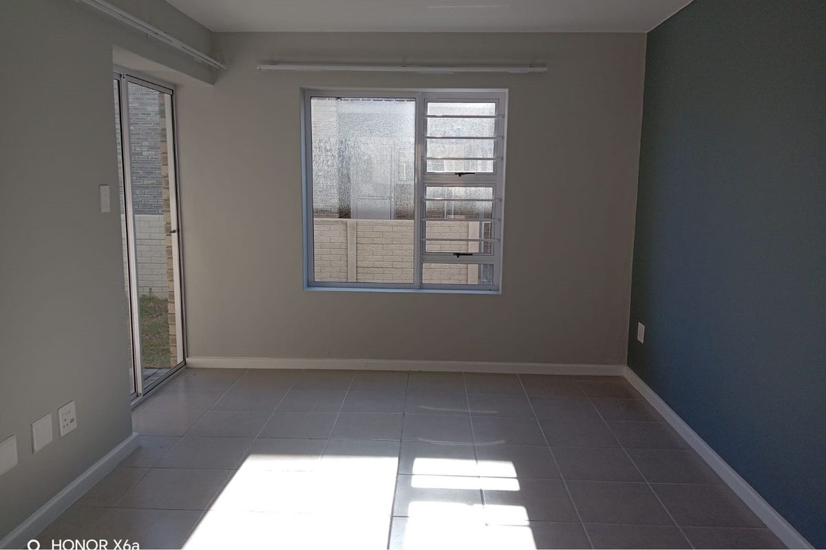 An empty living room featuring neutral tiled flooring, an accent wall, and natural light through an aluminium sliding door and window.
