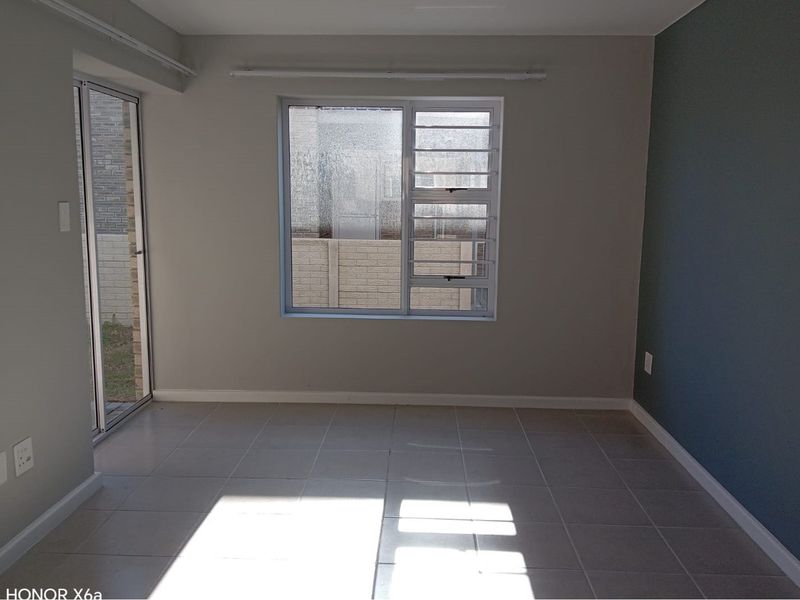 An empty living room featuring neutral tiled flooring, an accent wall, and natural light through an aluminium sliding door and window.