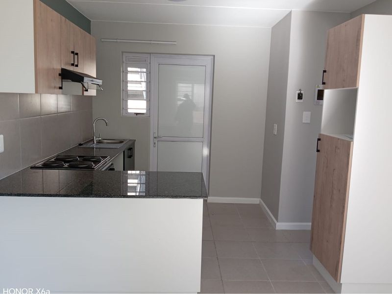 Modern kitchen featuring light wood-tone cabinetry, granite countertops, integrated hob, extractor fan, and tiled flooring with direct access to an exterior door.