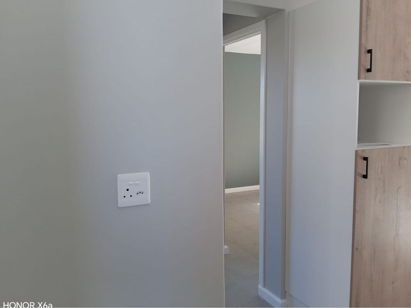 A clean, modern hallway featuring neutral wall tones, tiled flooring, and built-in cabinetry with wood-finish doors.