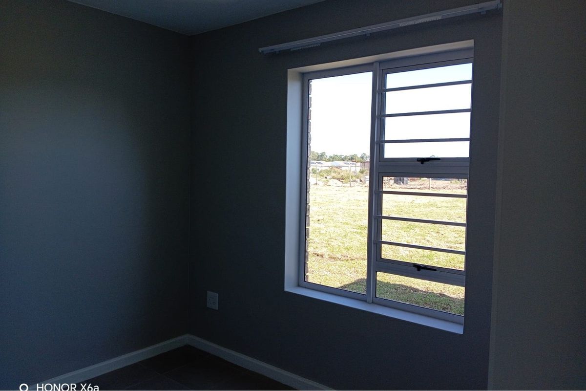 A clean, empty bedroom featuring dark grey walls, tiled flooring, and an aluminium window with integrated security bars.