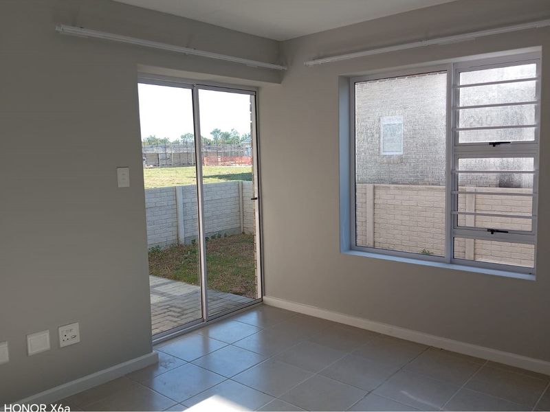 A bright, empty living area featuring neutral tiled flooring, a sliding glass door leading to the patio, and large windows with security bars.