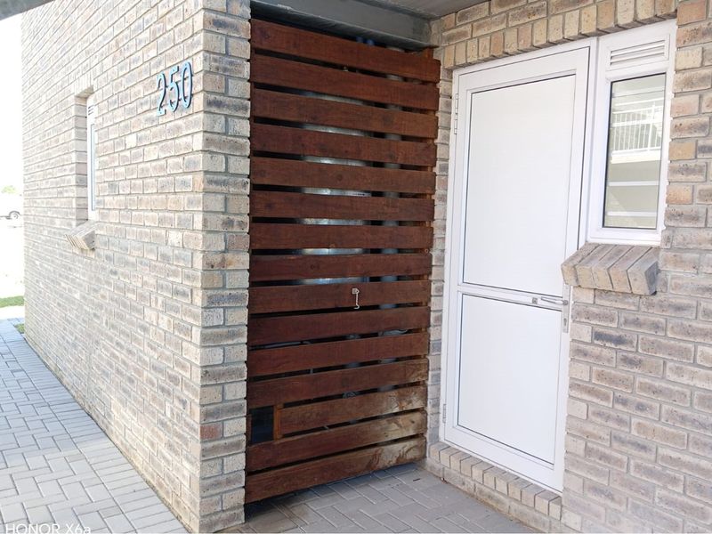 Front entrance of the townhouse featuring face brick construction, a timber privacy screen, and a secure uPVC door and window.