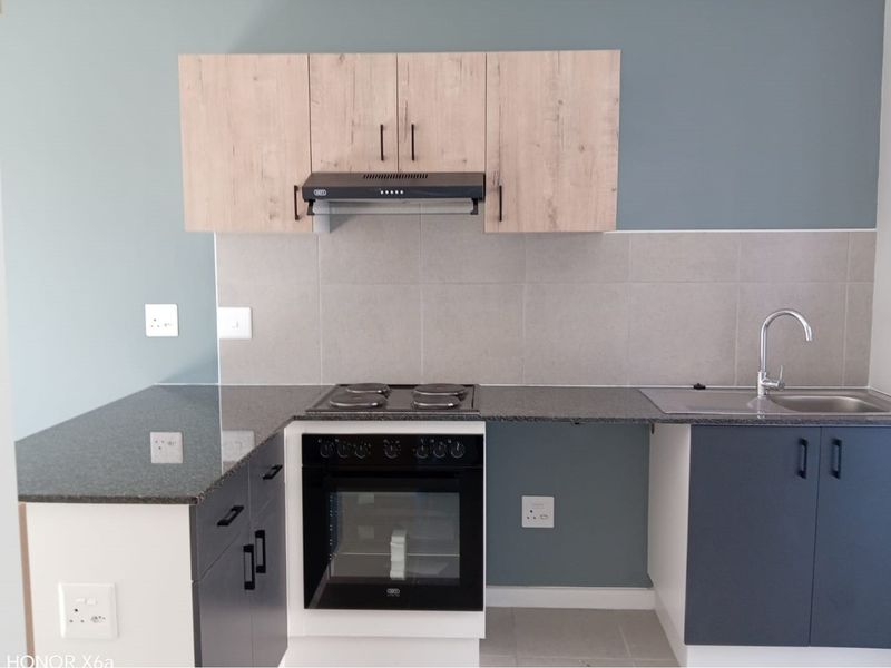 A modern, clean kitchen featuring two-tone cabinetry, granite countertops, a built-in oven and hob, and a stainless steel sink with a tiled splashback.