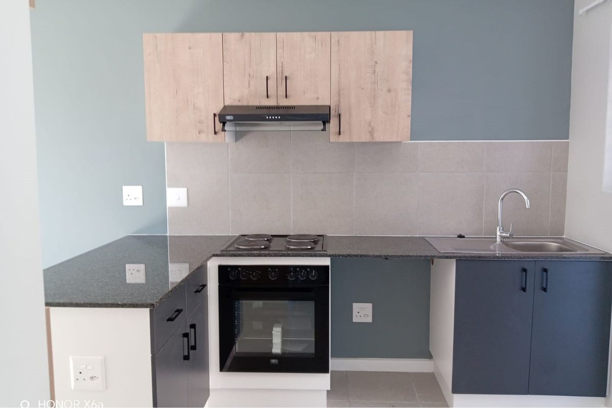 A modern, clean kitchen featuring two-tone cabinetry, granite countertops, a built-in oven and hob, and a stainless steel sink with a tiled splashback.
